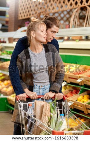 Young couple at the supermarket doing daily shopping walking with cart hugging choosing vegetables pensive just walk out shopping technology Royalty-Free Stock Photo #1616633398