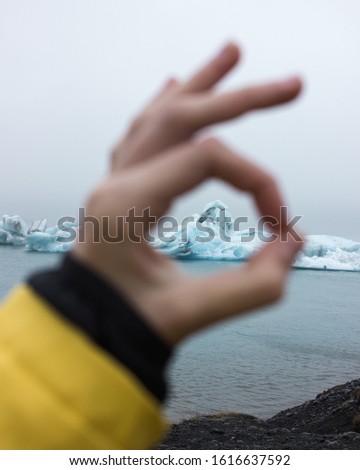 Looking at an iceberg floating in Iceland's Glacier Lagoon through the hand of a young girl wearing a yellow raincoat.