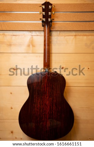 Backside of an acoustic guitar hanging on a wood panel wall