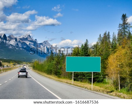 Classic green traffic information sign. Road sign for information or map. Blank board with place for text. Highway against Canadian Rocky Mountains.