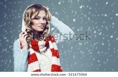 beautiful smiling blonde wearing a woolen sweater and knitted scarf against snow 