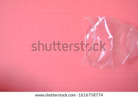 Wrinkled Translucent Plastic Cup, in a Coral Paper Background. Zero-waste and Plastic free Conceptual Photography.