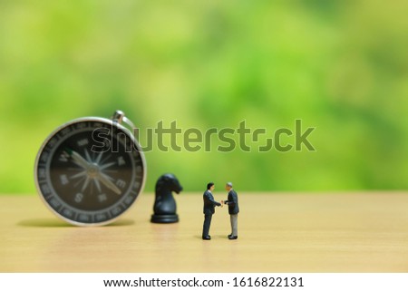Miniature people strategic concept - businessman make partnership strategy in front of horse knight pawn and compass