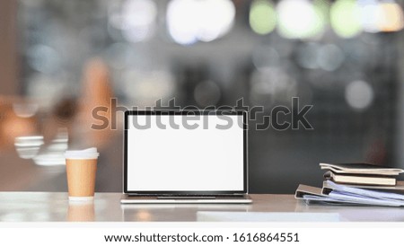 Laptop with white blank screen on white table with coffee cup and document file. Home interior or office background.