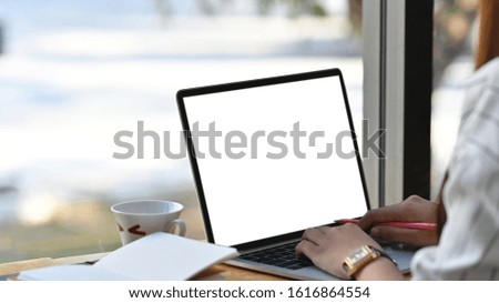 Close-up image of beautiful business woman sitting at the wooden work desk and typing on the white blank screen laptop keyboard.