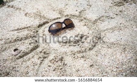 Sunny happy face wearing sunglasses drawn in the sand on the beach