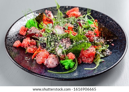 Italian Cuisine. Seafood salad with octopus, lettuce, grapefruit, green moss, black and white sesame seeds, red pepper. background image, copy space text