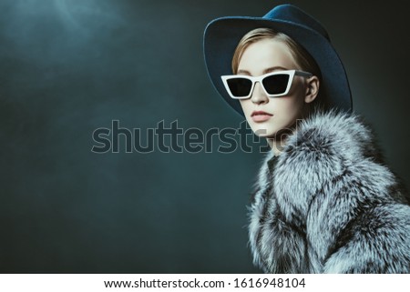 A portrait of a young fashionable woman in a hood and sunglasses. Beauty, optics, fashion.