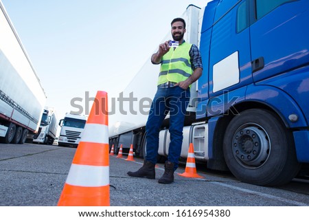 Portrait of middle aged bearded truck driver standing by his truck and showing his commercial driver license. Truck driving school and job openings. Royalty-Free Stock Photo #1616954380