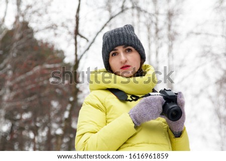 Young woman with a camera in a winter park on a background of trees. A girl photographer holds a camera in hand. Women hobbies. Copy space
