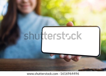 Mockup image of a woman holding and showing black mobile phone with blank desktop screen 