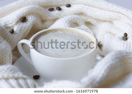 White coffee cup with plate, cofee beans and knitted scarf. Comfort and relax concept.