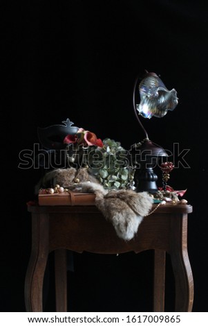A picture inspired  Netherlands still-life painting, shows jewelry, fur scarf, flowers and a old-styled glass lamp on a wooden table.