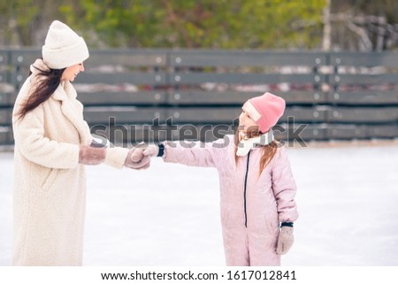 Little adorable girl with her mother skating on ice-rink. Family winter fun