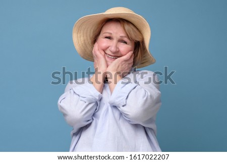 Beautiful senior woman in summer hat looking with smile at camera pleased to hear a compliment to her flowers. Studio shot