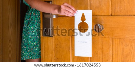female hand hangs a sign on the door do not disturb in hotel.