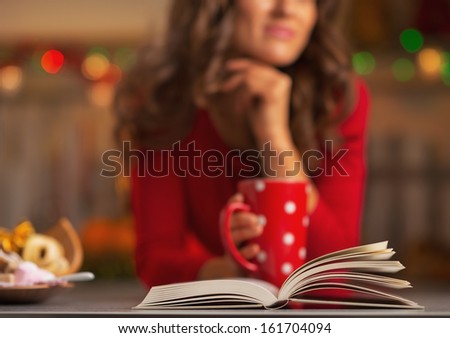 Closeup on book and thoughtful young woman with cup of hot chocolate in background