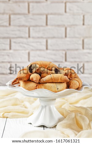 freshly baked mini croissants with poppy seeds and raisins filling on a white cake stand on a concrete table with a brick wall at the background, close-up, vertical view 