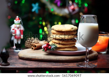 Cookies biscuits for Santa Claus near a christmas tree decorated with Nutcracker, flashing lights,mistletoe and a glass of milk on a wooden tray, atmospheric Christmas picture 