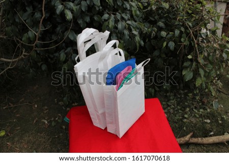 White Bags Isolate on Lush Lava 2020 Trends Color Table against green plant leaves. Eco Friendly Non Woven Shopping Recyclable Bags. Environmentally Concept. Reusable Grocery Bags. Reduce, Reuse,
