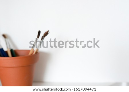 A pot of artists paint brushes in a browm pot on a white background. Copy space available.