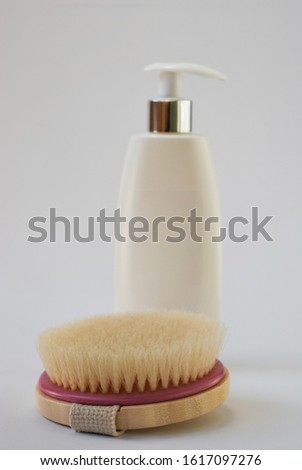 A brush for a dry massage from a tree. Against a blurry background, a white bottle with cosmetics, gold framing and a dispenser