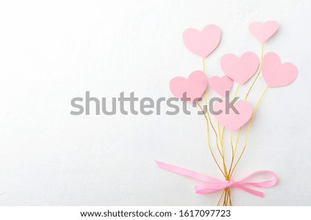 Bouquet of pink paper hearts on the golden wire and pink ribbon bow on the white surface.Empty space for design
