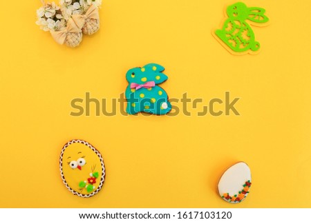 Handmade multi-colored gingerbread cookies in the form of a bunny and Easter eggs, straw shoes and flowers on a yellow background. Gingerbread Easter Bunny, decoration