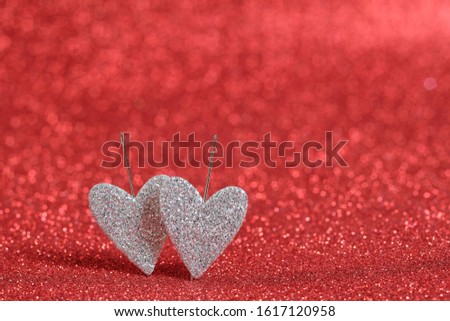 Two silver hearts on a red bokeh background. Hearts are pierced to the background with needles. Picture for Valentine's Day and wedding. Bokeh red background and copy space