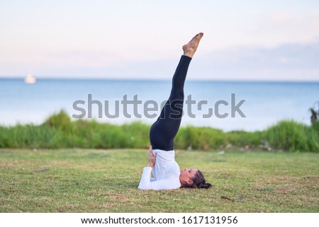 Young beautiful sportwoman practicing yoga. Coach teaching shoulder stand pose at park