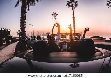 Happy people having fun in convertible car in summer vacation at sunset - Young couple enjoyng  holiday on cabriolet auto outdoor - Travel, youth lifestyle and wanderlust concept - Focus on hands Royalty-Free Stock Photo #1617150085