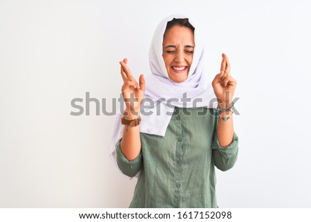 Young beautiful Arab woman wearing traditional Muslim hijab over isolated background gesturing finger crossed smiling with hope and eyes closed. Luck and superstitious concept.