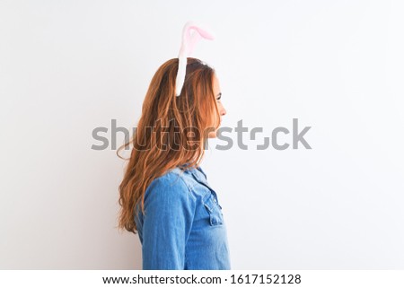 Young redhead woman wearing easter bunny ears over isolated background looking to side, relax profile pose with natural face with confident smile.