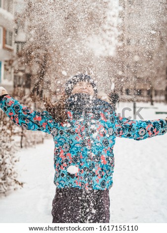 The girl runs through the snowy streets of the city, frolics in snowdrifts, the first snow
