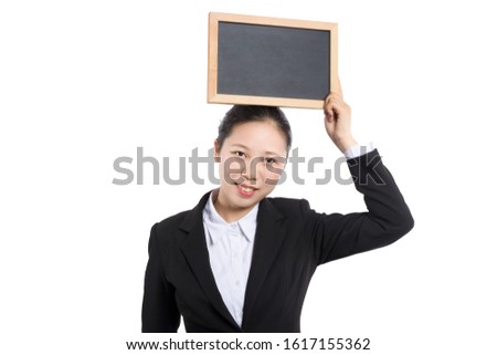 Portrait of a teacher in a classroom. The teacher stands at the blackboard with a textbook in one hand, holds his thumb up and looks away.