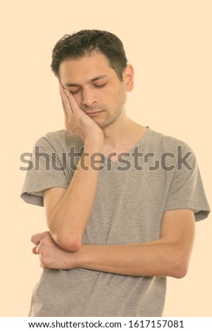 Studio shot of tired young man sleeping while resting face on hand