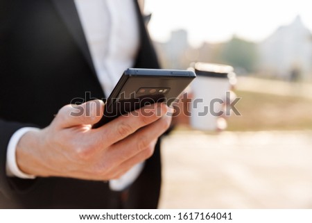Close up of a businessman using mobile phone outdoors, holding takeaway coffee cup
