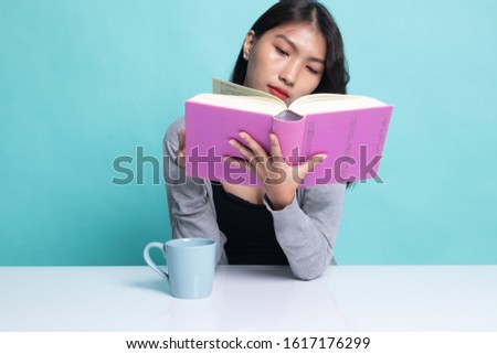 Young Asian woman read a book with cup of coffee on cyan background.