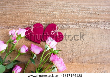 Small pink roses and two red wooden hearts on a background of unpainted and untreated boards. Valentine's day composition, selective focus.