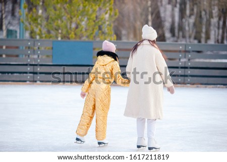 Little adorable girl with her mother skating on ice-rink. Family winter fun