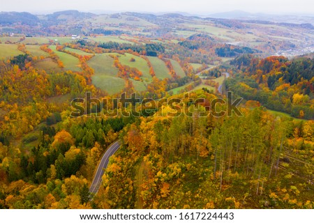View from drone of undulating forest landscape with curving road on autumn day

