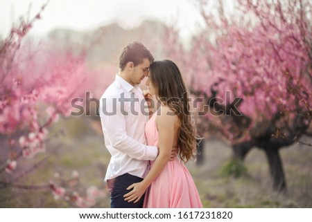 Romantic bridegroom kissing bride on forehead while standing against wall covered with pink flowers.