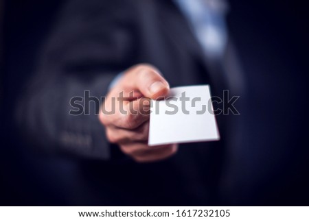 Businessman in suit holding in hand business card in front of black background