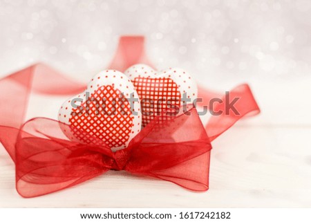 Love composition with two hearts and a red bow on a light bokeh background.