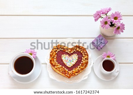 Top view on a festive table with a heart-shaped homemade cake, two cups of coffee, a gift and a bouquet of flowers. Beautiful congratulations on Valentine's Day or Happy Birthday. Flat lay, copy space