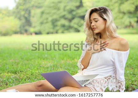 A Beautiful Caucasian woman sitting on green grass in a park and using laptop computer for online shopping or working or network communication chatting in vacation day