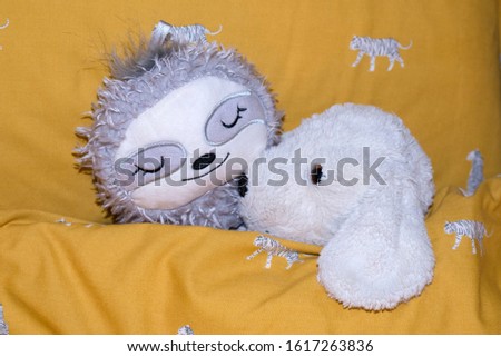 Cuddly teddies in bed including a furry sloth hot water bottle and a white fluffy dog toy