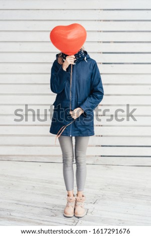 Vertical image to valentine's day. Hipster woman on white wooden background with a red heart-shaped balloon. unrecognizable concept