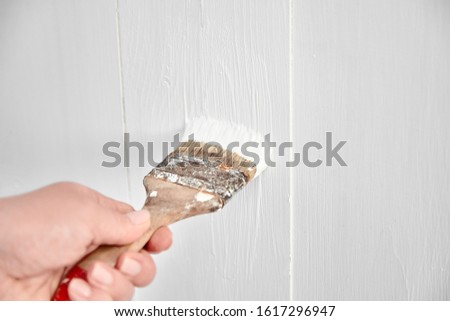 Painting work. Woman paints a wooden surface wall with white acrylic paint. Female hand with brush. Home repair