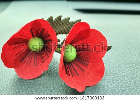 The bright red poppy brooch is placed on a black leather floor. Considered as a veteran's day flower, To commemorate the soldiers who dedicated their lives to protect their beloved fatherland.